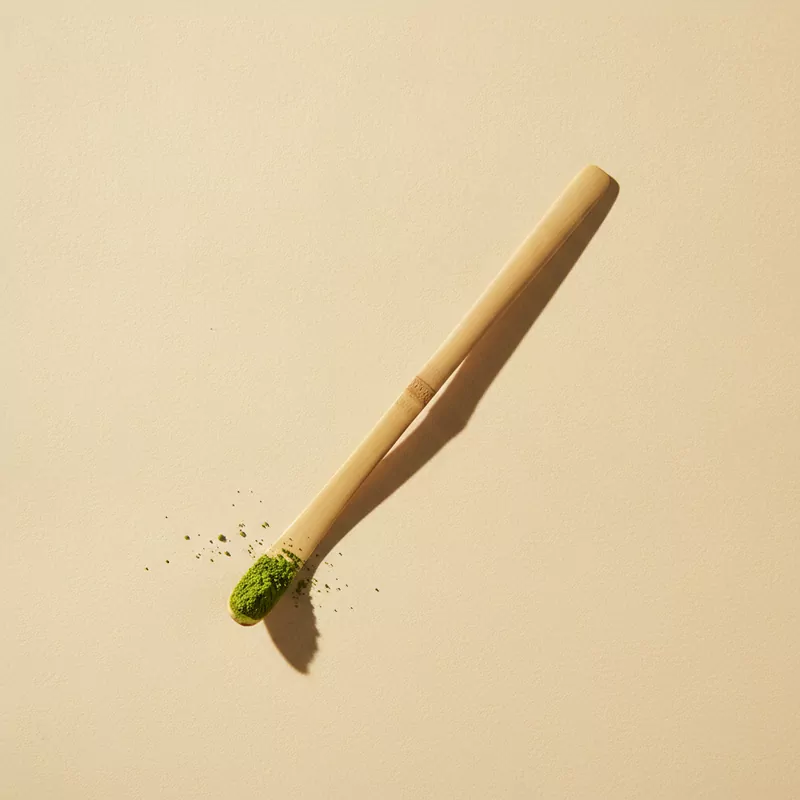 Schlanker Bambuslöffel mit einem Häufchen grünem Matcha-Pulver an der Spitze